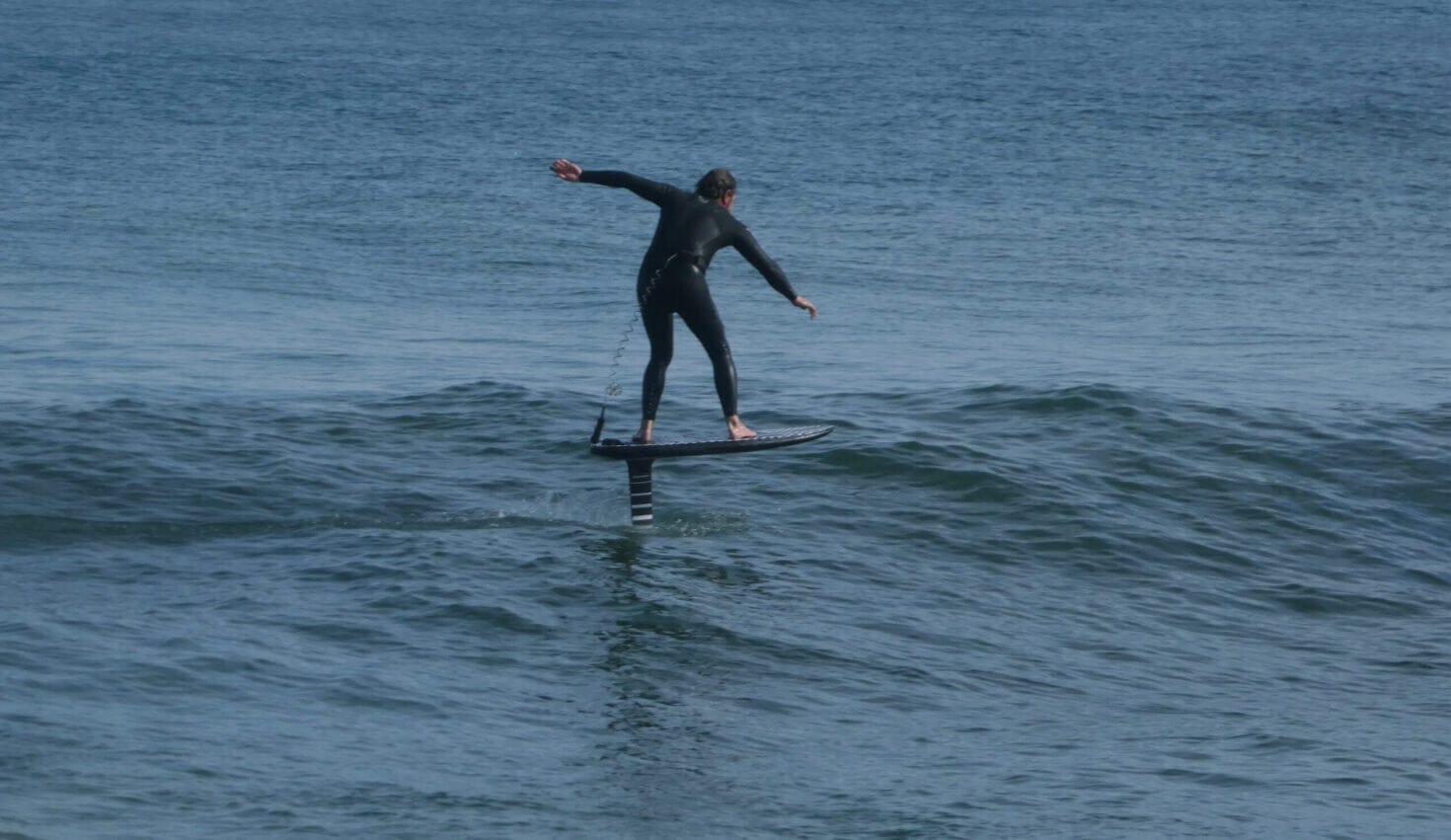 rear view of man wearing wetsuit surfing on hydrofoil board Los mejores lugares para utilizar el eFoil en Baleares